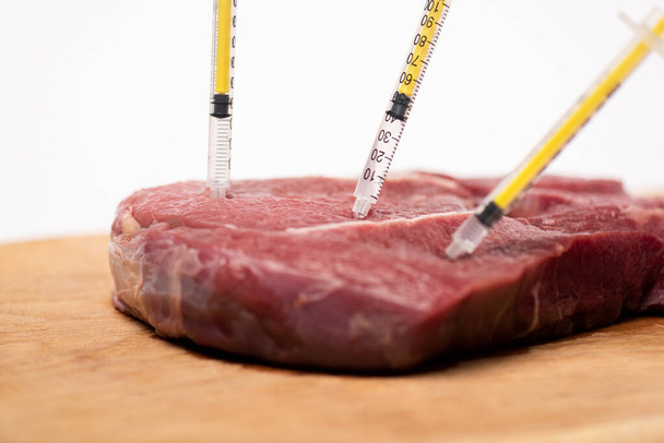 Enfoque selectivo de jeringas en carne cruda sobre tabla de cortar aislada en blanco
 - Foto, Imagen