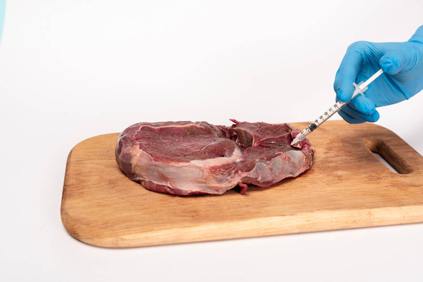 Обрізаний вид лікаря зі шприцом робить гормональне введення в сире м'ясо на обробній дошці ізольовано на білому
 - Фото, зображення
