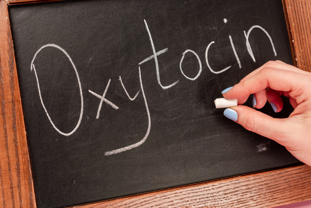 Cropped view of woman holding piece of chalk near blackboard with oxytocin lettering - Foto, imagen