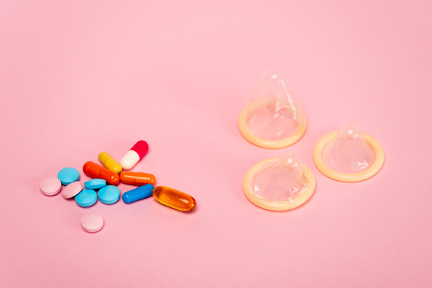Close up view of condoms and birth control pills on pink background - Photo, Image