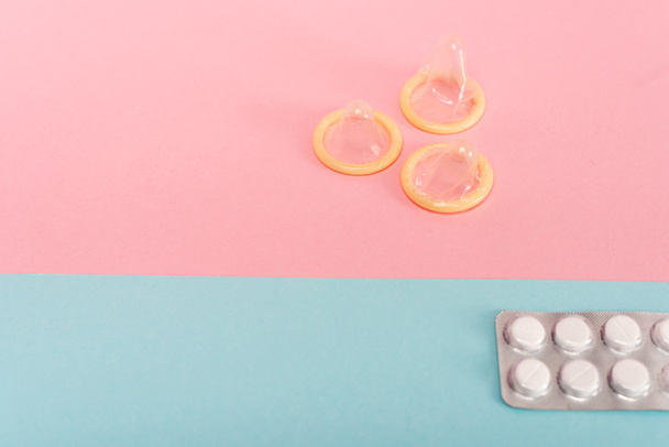 Hoge hoek uitzicht van condooms en anticonceptiepillen op roze en blauwe oppervlak - Foto, afbeelding