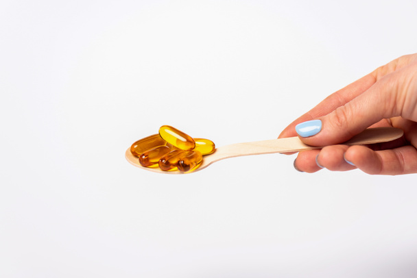 Cropped view of woman holding wooden spoon with pills of omega 3 isolated on white - Foto, Bild