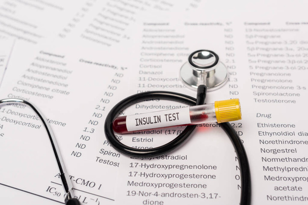 Close up view of stethoscope and test tube with insulin test lettering on lists with hormones  - Фото, изображение
