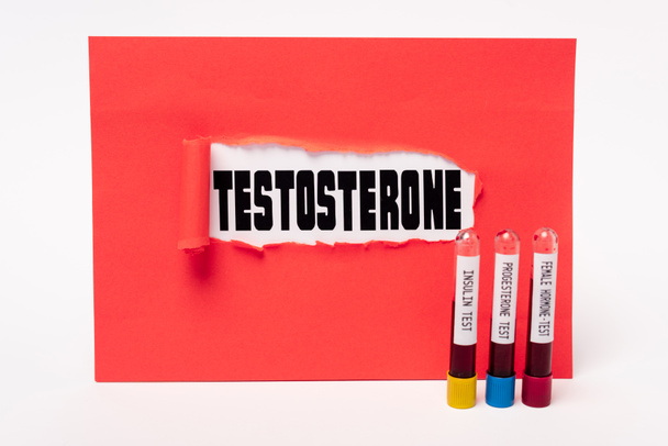 Napis testosteronu w otworze z czerwonego papieru i probówek z próbkami krwi insuliny, progesteronu i hormonów żeńskich na białym tle - Zdjęcie, obraz