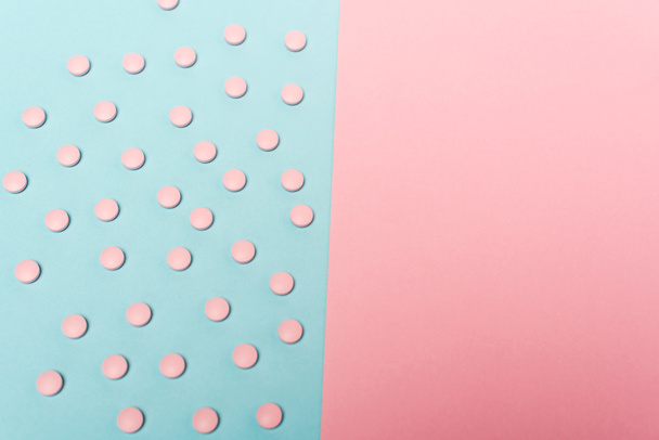 Hoge hoek weergave van hormonale pillen op blauw oppervlak in de buurt van roze achtergrond - Foto, afbeelding