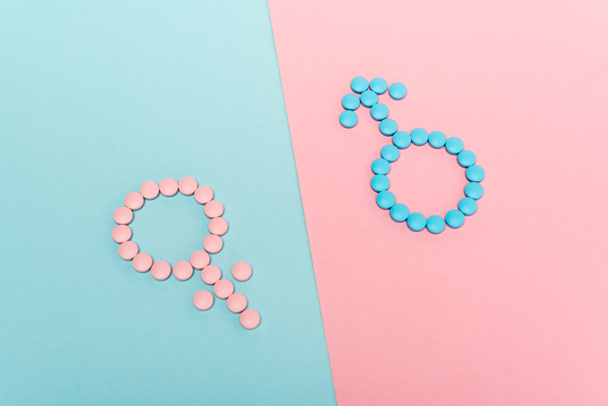 Hochwinkelaufnahme weiblicher und männlicher Zeichen aus Hormontabletten auf blauem und rosa Hintergrund - Foto, Bild