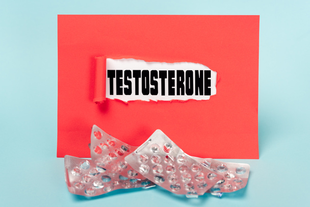 Paper with testosterone lettering and empty blisters of pills on blue background - Foto, imagen