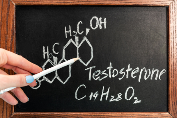 Cropped view of woman holding pencil near blackboard with testosterone formula - Photo, Image