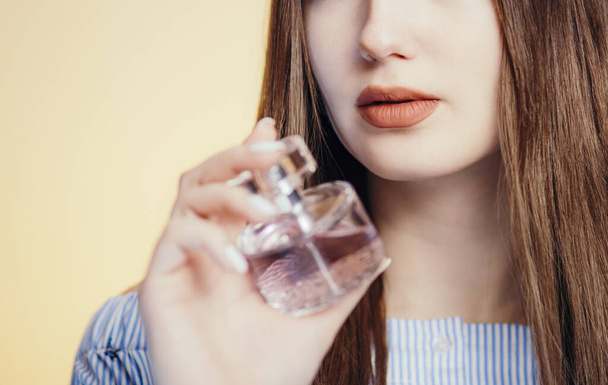 perfume bottles in the hands of a beautiful girl on a studio color background, part of the face of a young woman with aroma, concept of care and cosmetics - Fotografie, Obrázek