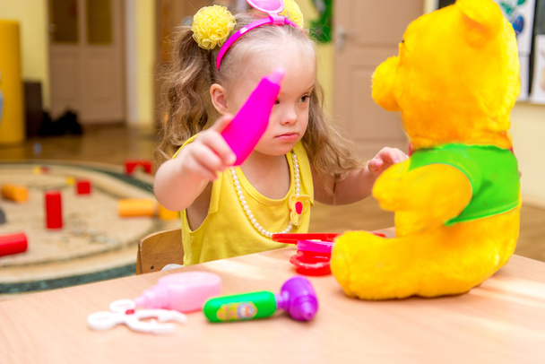 Meisje met down syndrom spelen arts met speelgoed beer, revalidatiecentrum - Foto, afbeelding