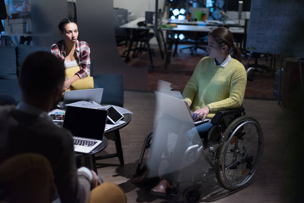Handicapped young woman with colleagues working in office. She is smiling and passionate about the workflow. Performing in co-working space. Office people working together. - Photo, Image