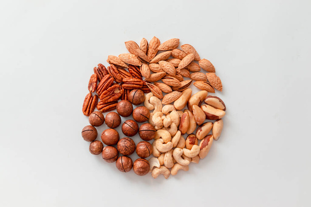 Assorted brown nuts circle on a gray background. Macadamia, cashews, minced almonds, pecans, wholesome food - Photo, Image