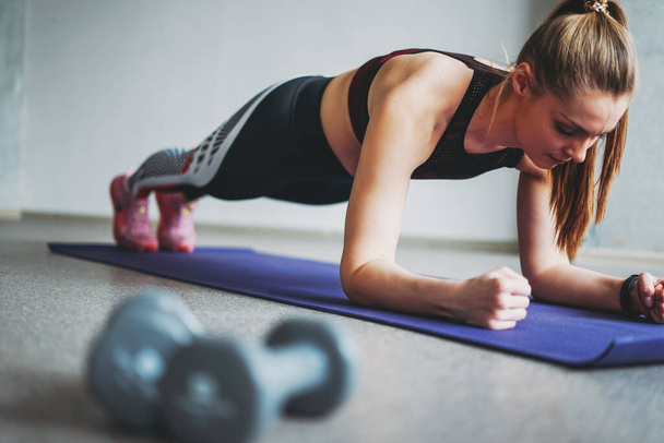 Attractive fit young woman in sport wear girl trains with dumbbells make plank at the loft studio - Foto, imagen