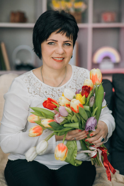 Woman holding tulips and smiling to the camera. Beautiful Woman In Nice Spring Bouquet Of Tulips. Woman showing a bunch of assorted flowers. Smiling woman with bunch of flowers - Фото, изображение