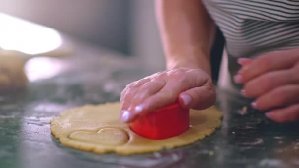Female hand makes hearts out of dough, close-up view. Hostess  preparing hearts from dough for baking cookies. Woman cooking food on the kitchen, at home. 4k Slow motion footage  - Imágenes, Vídeo