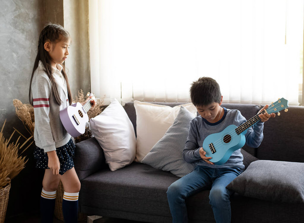 Two children playing ukulele together,with happy feeling,at home studio,beside window,blurry light around - Foto, Imagen