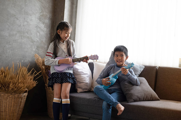 Двоє дітей грають на укулеле разом, з щасливим почуттям, вдома, біля вікна, розмите світло навколо - Фото, зображення