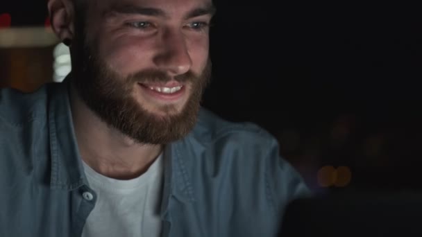 A close-up view of a young man is sitting in front of his laptop computer at night time - Záběry, video