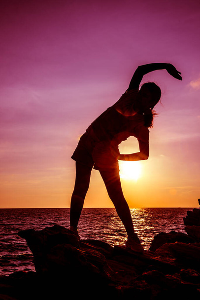 Sylwetka kobieta ćwiczenia na plaży zachód słońca. Sport i zdrowy styl życia. - Zdjęcie, obraz