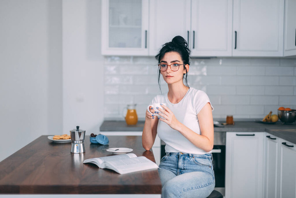 Beautiful young woman drinking coffee in the kitchen - 写真・画像