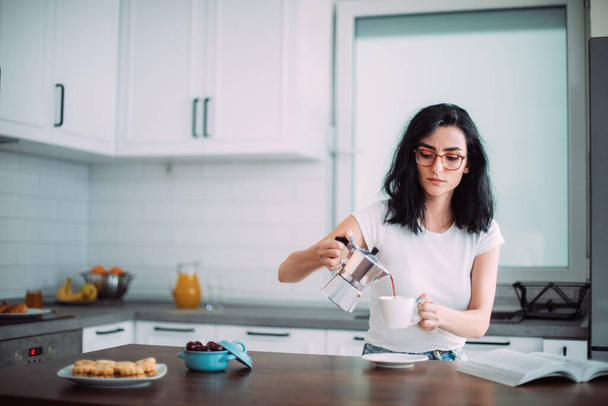 Beautiful young woman pouring coffee in the kitchen - Foto, Bild