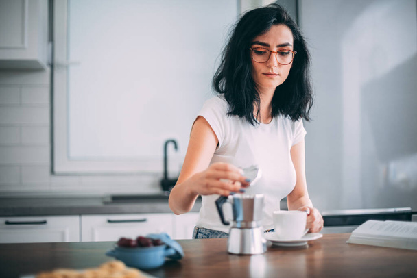 Beautiful young woman pouring coffee in the kitchen - Photo, image