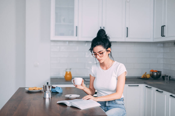 Beautiful young woman reading book in the kitchen - 写真・画像