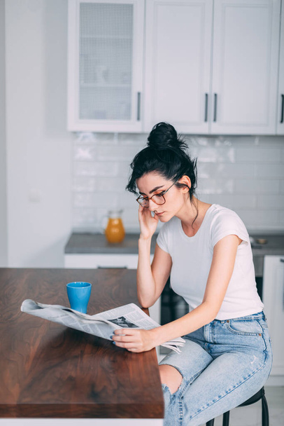 Beautiful young woman reading newspaper in the kitchen - Photo, image