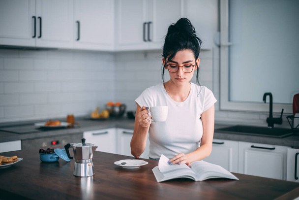 Beautiful young woman reading book in the kitchen - Foto, imagen