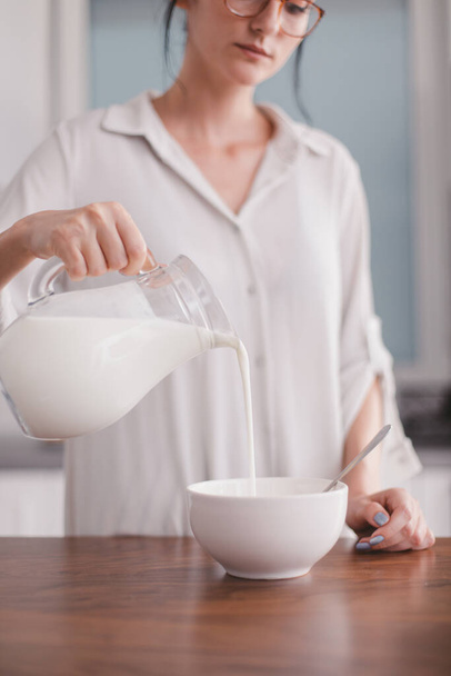 Beautiful young woman pouring milk in a bowl - Foto, Bild