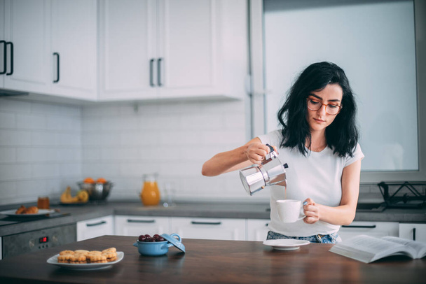 Beautiful young woman pouring coffee in the kitchen - Fotoğraf, Görsel