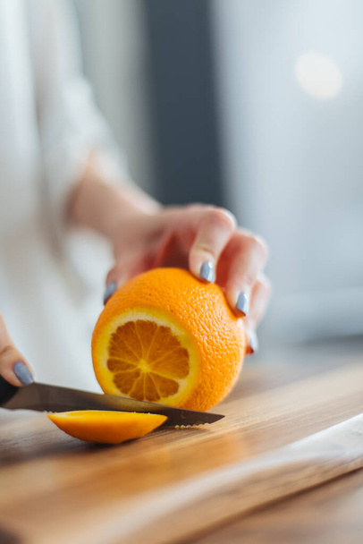 Beautiful young woman cutting orange on the kitchen counter - 写真・画像