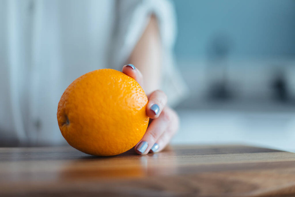 Close-up shot of a girl's hand holding orange on a kitchen counter - Foto, Bild