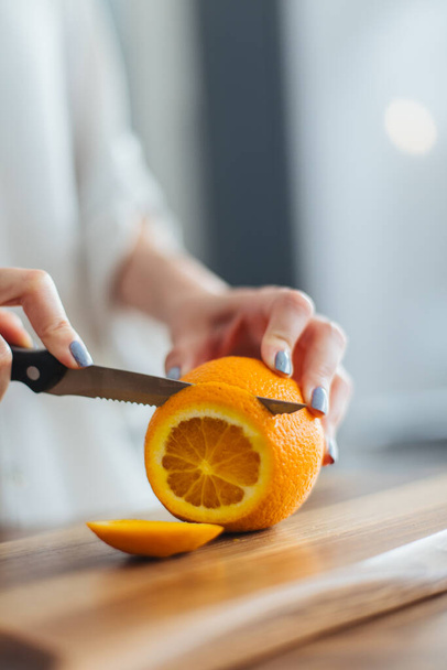 Beautiful young woman cutting orange on the kitchen counter - Foto, afbeelding