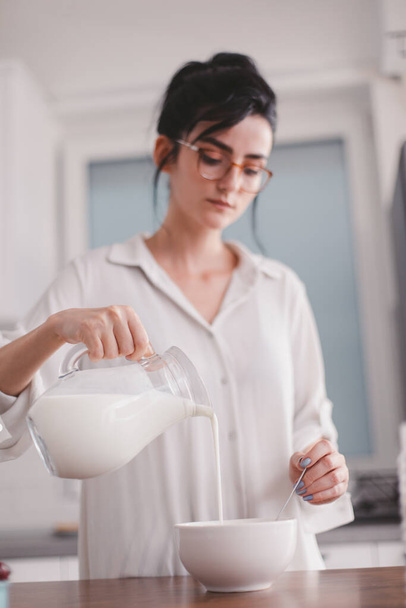 Beautiful young woman pouring milk in a bowl - Foto, imagen
