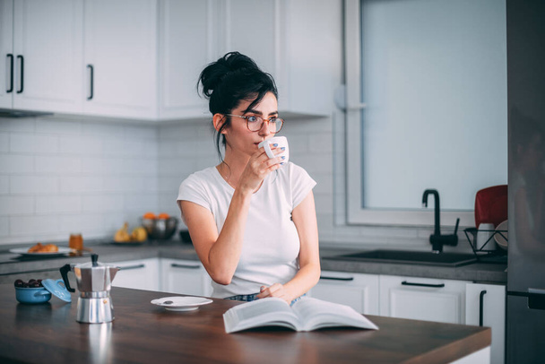 Beautiful young woman drinking coffee in the kitchen - Фото, зображення