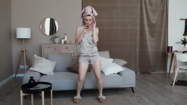 Attractive girl dressed in nightwear and slippers, wearing wireless headphones - Filmagem, Vídeo