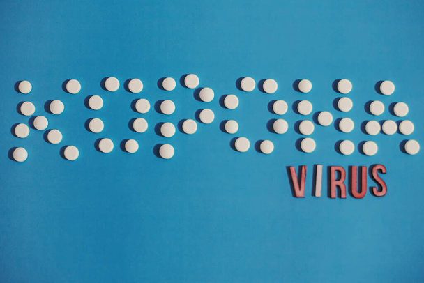 Tekst Corona virus in Oekraïense letters van witte tabletten en houten letters op blauwe achtergrond. Nieuwe Coronavirus uitbraak concept. 2019-nCoV virusinfectie van oorsprong uit Wuhan, China. - Foto, afbeelding