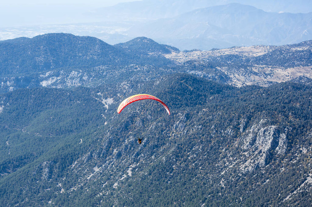KEMER, TURKEY - OCTOBER 22, 2017: Paraglider flying over mountains near Kemer, a seaside resort on the Turkish Riviera in Antalya Province, Turkey - 写真・画像