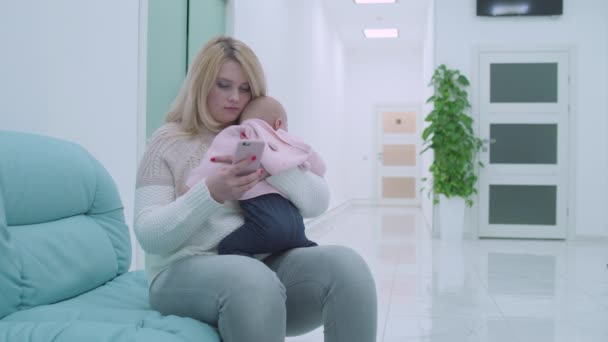 Young female visiting doctor in clinic, holding infant baby in arms, medicine - Materiał filmowy, wideo