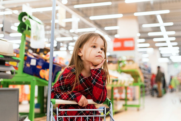Tramvayı olan sevimli bir bebek marketten taze sebze seçiyor. Satış, tüketim ve insan konsepti - markette alışveriş arabasında yiyecek taşıyan mutlu küçük kız. - Fotoğraf, Görsel