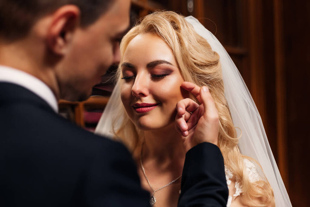 die Braut mit dem schönen Make-up schloss die Augen und der Bräutigam berührte ihr Gesicht mit der Hand. - Foto, Bild