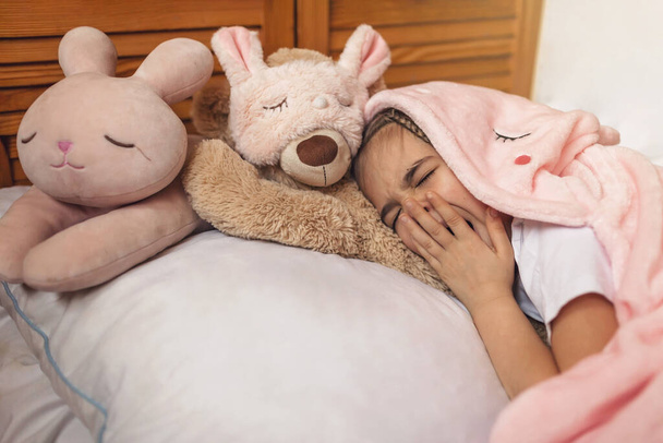 Horní pohled na roztomilé probuzení školní dívka se svými hračkami zvířata nosit v světle růžové pyžamo s jednorožec hoody, šťastný rodinný koncept, vnitřní horizontální portrét - Fotografie, Obrázek