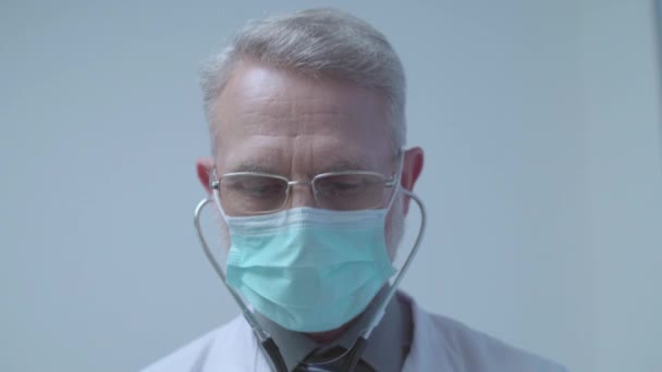 Medical specialist in mask with stethoscope examining patient, clinic check-up - Materiał filmowy, wideo