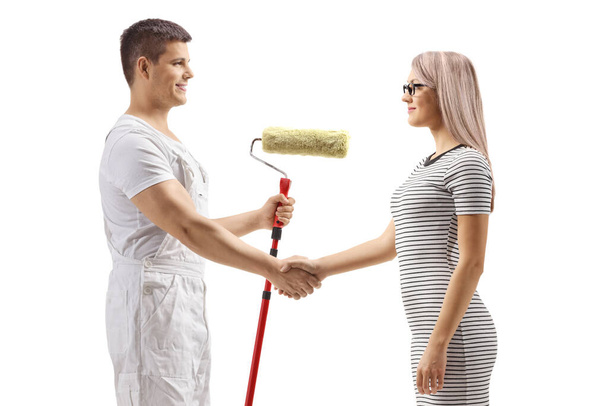 Male worker with a roller painter shaking hands with a young woman isolated on white background - Foto, imagen
