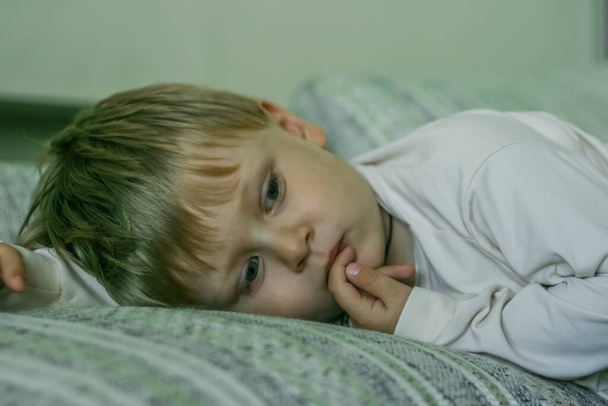 2011.09.06, Maloyaroslavets, Rusko. portrét malého světlovlasého smutného chlapce ležícího na pohovce a sledujícího televizi. - Fotografie, Obrázek
