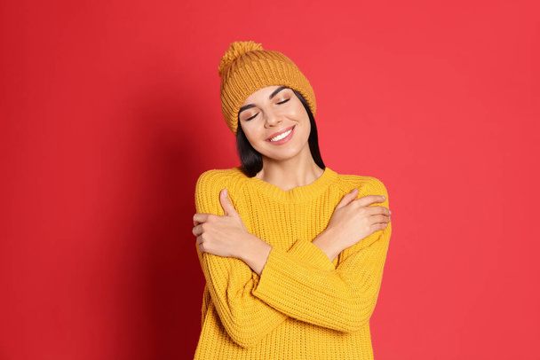Young woman wearing warm sweater and hat on red background. Winter season - Photo, image