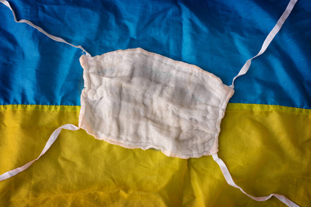 Reusable gauze surgical protective mask on a blue-yellow background resembles the Ukrainian flag. Pandemic in Ukraine - Photo, Image