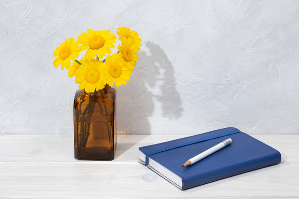 Kauniita kukkia pullossa ja sininen päiväkirja puupöydällä. Kirjoittaminen tai piirustus käsite. Vapaa-aikaa. Kopioi tila
 - Valokuva, kuva