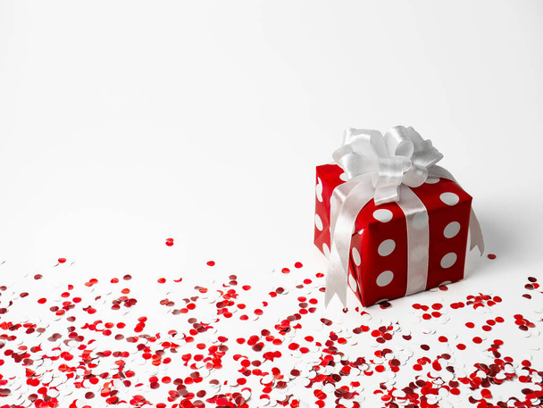 ajándék szilveszterre, karácsonyra, születésnapra, szerettekre. Piros polka pont doboz fehér íj fehér háttér konfetti. - Fotó, kép